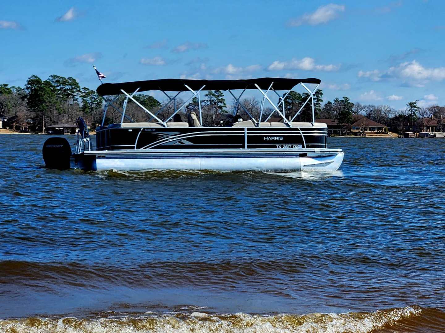 Pontoon boat on a lake near a sandy shore under a clear blue sky.