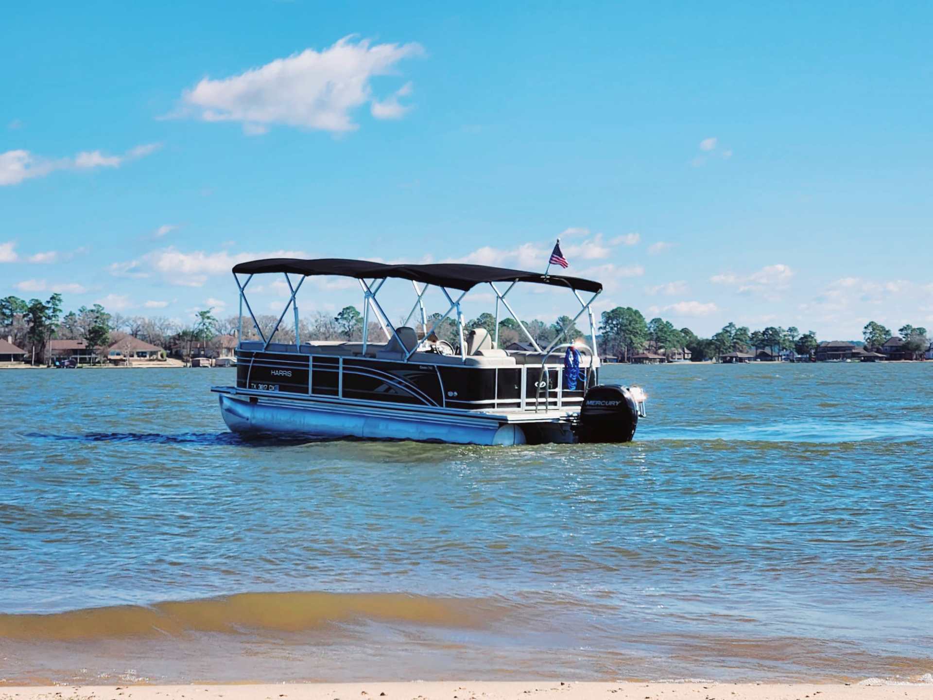 Pontoon boat with canopy on lake under a clear blue sky.