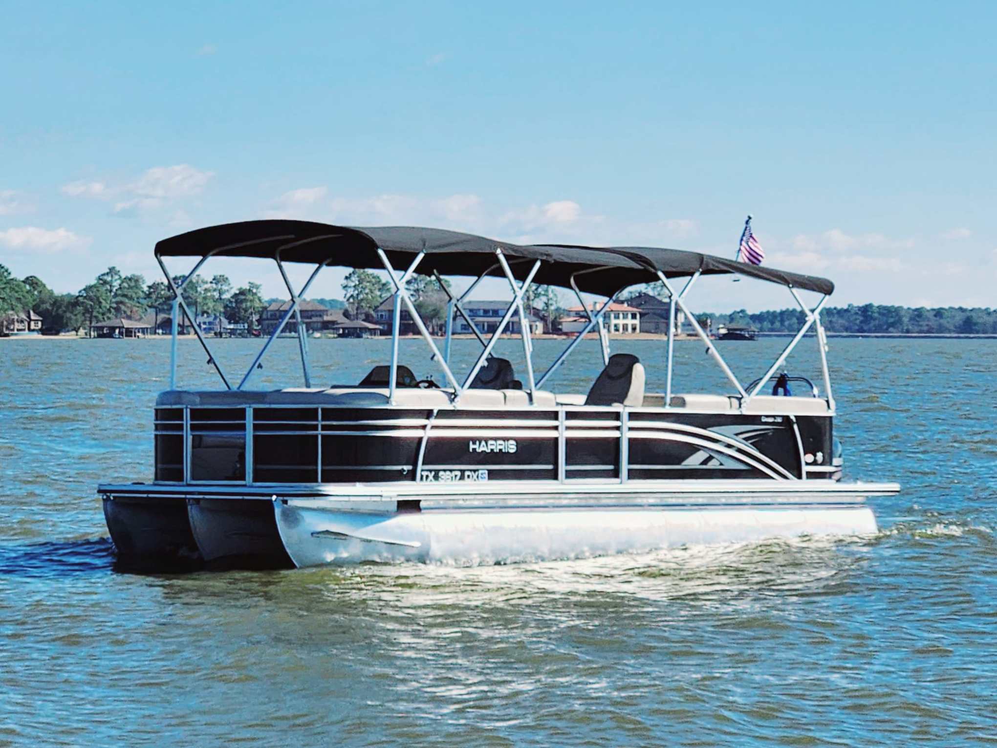 Pontoon boat with canopy on a lake, distant shore in background.