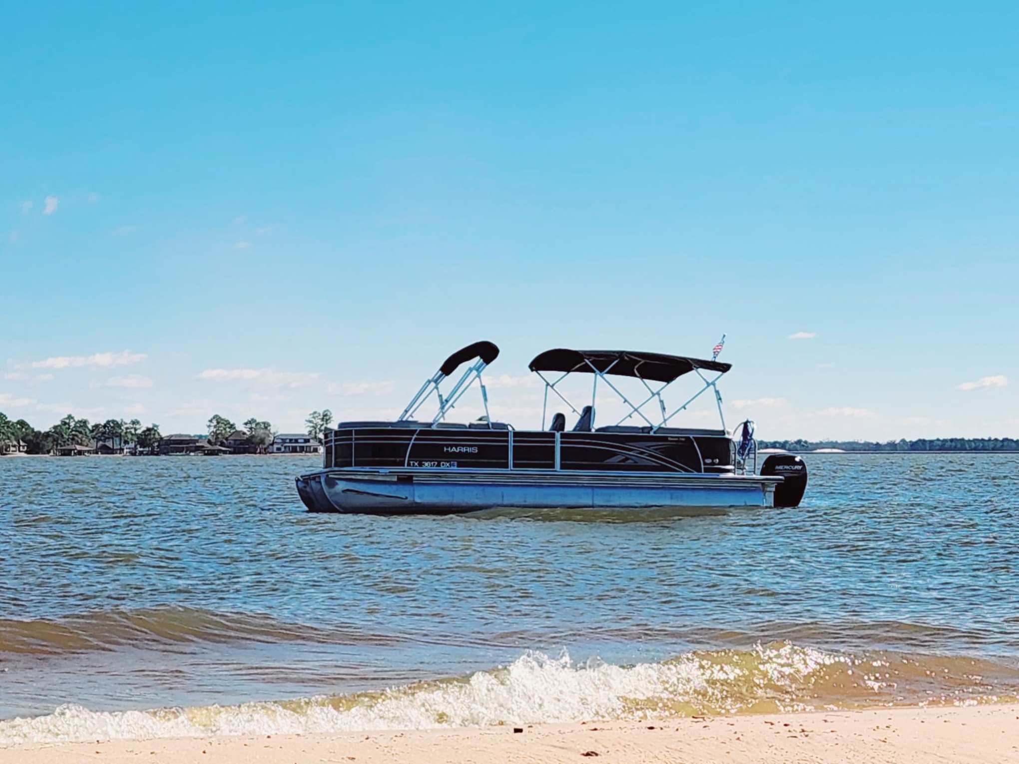 Pontoon boat on calm lake with clear blue sky in the background.