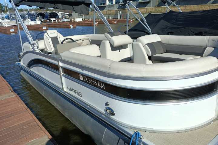 A white pontoon boat docked by the water with cushioned seating.