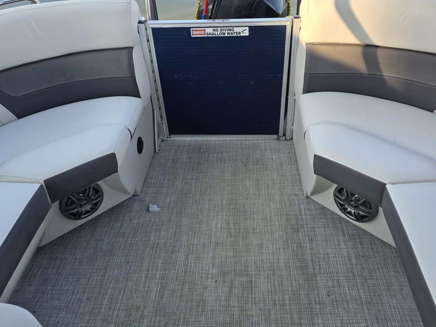Pontoon boat interior with seating, carpeted floor, and view of water.