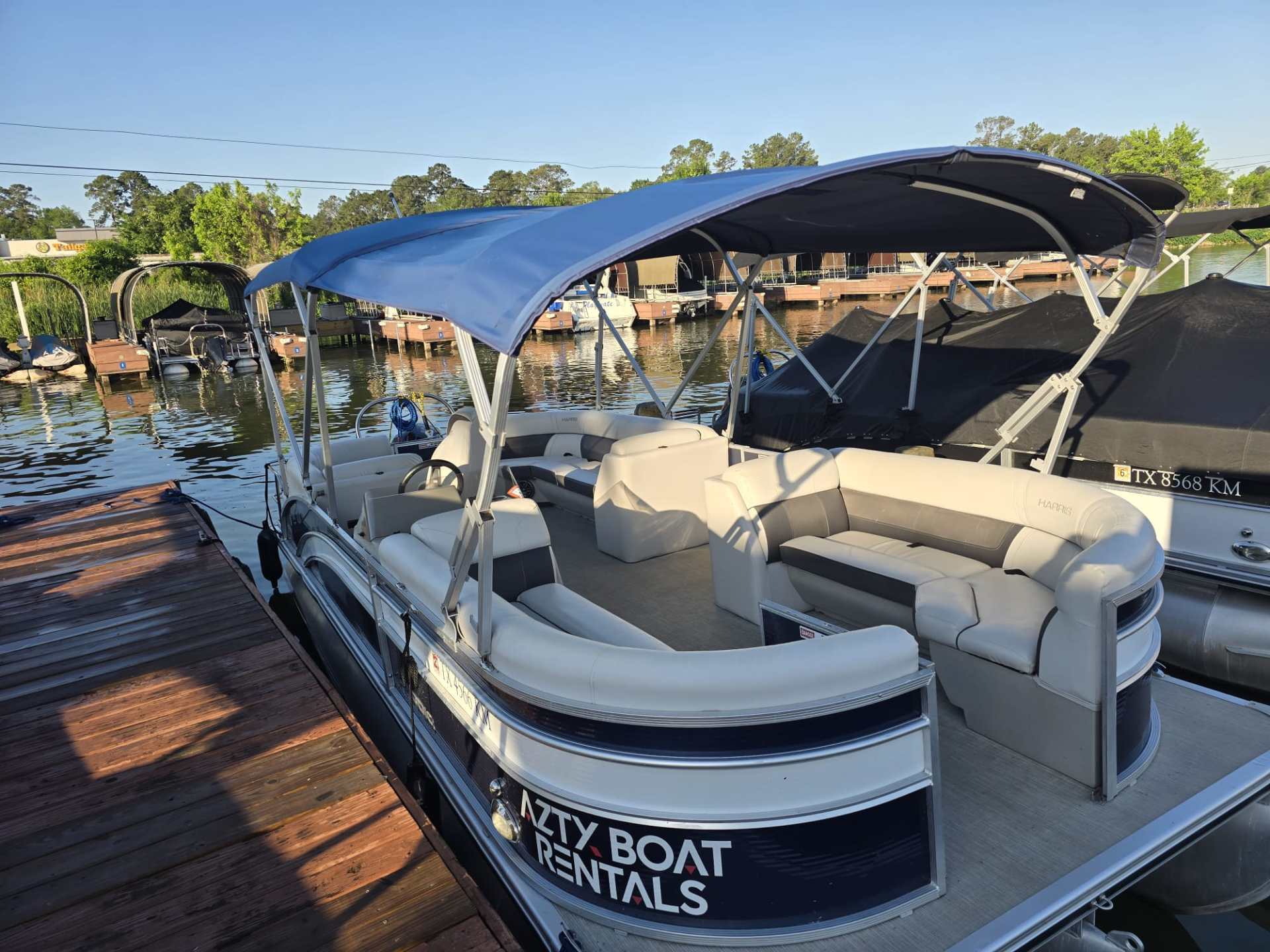 Pontoon boat with blue canopy docked near other boats on a sunny day.