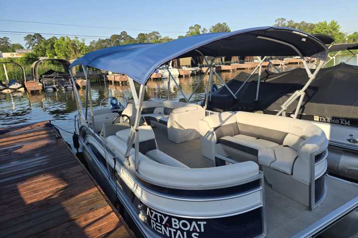 Pontoon boat with blue canopy docked near other boats on a sunny day.