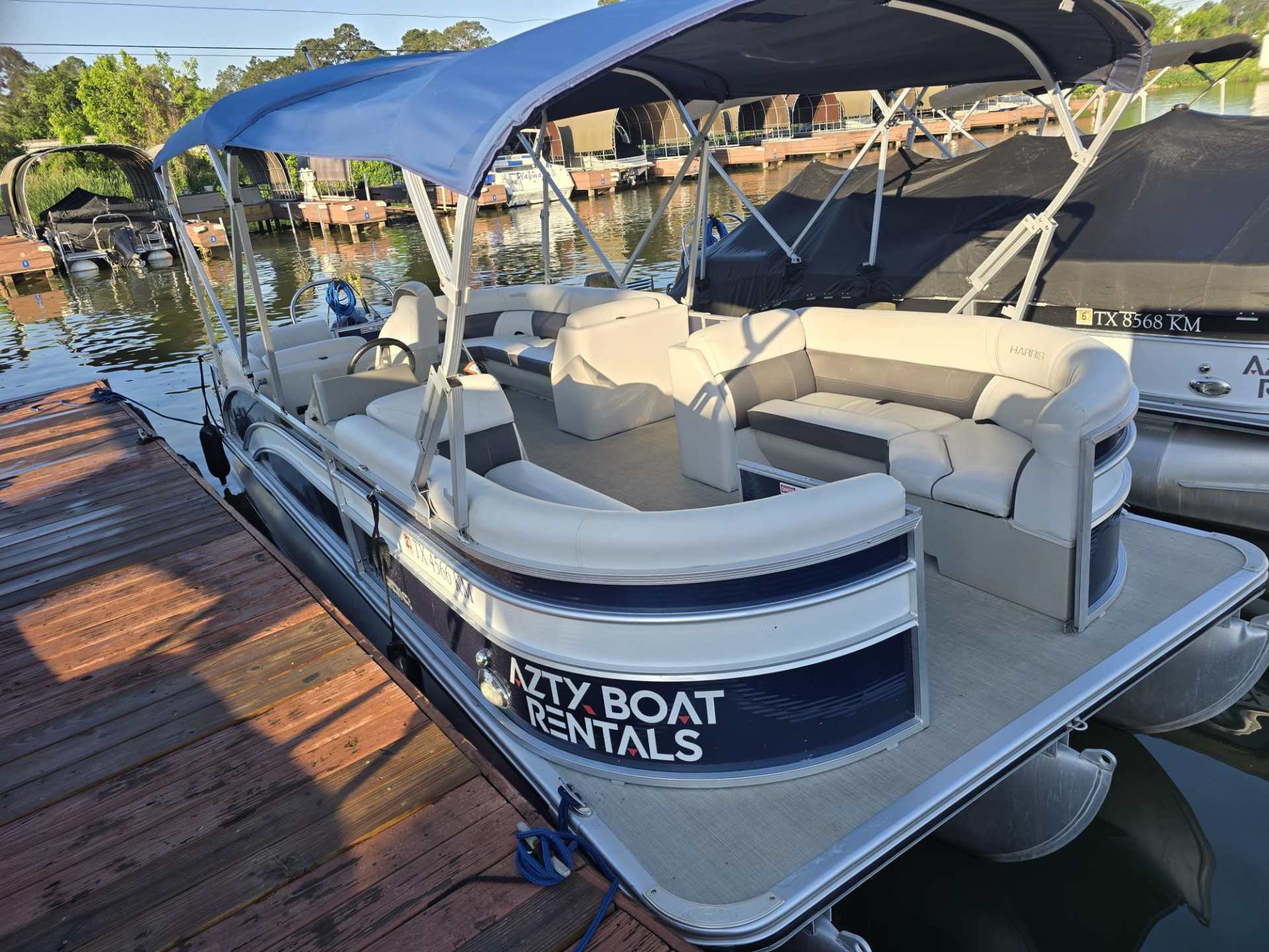Pontoon boat with blue canopy docked at marina.