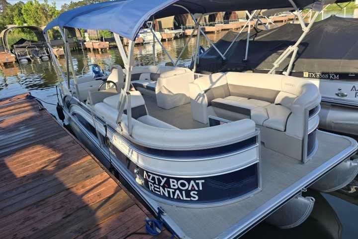 Pontoon boat with blue canopy docked at marina.