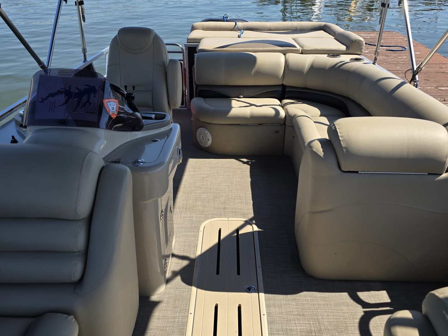Interior of a pontoon boat with beige seating, docked at a marina.