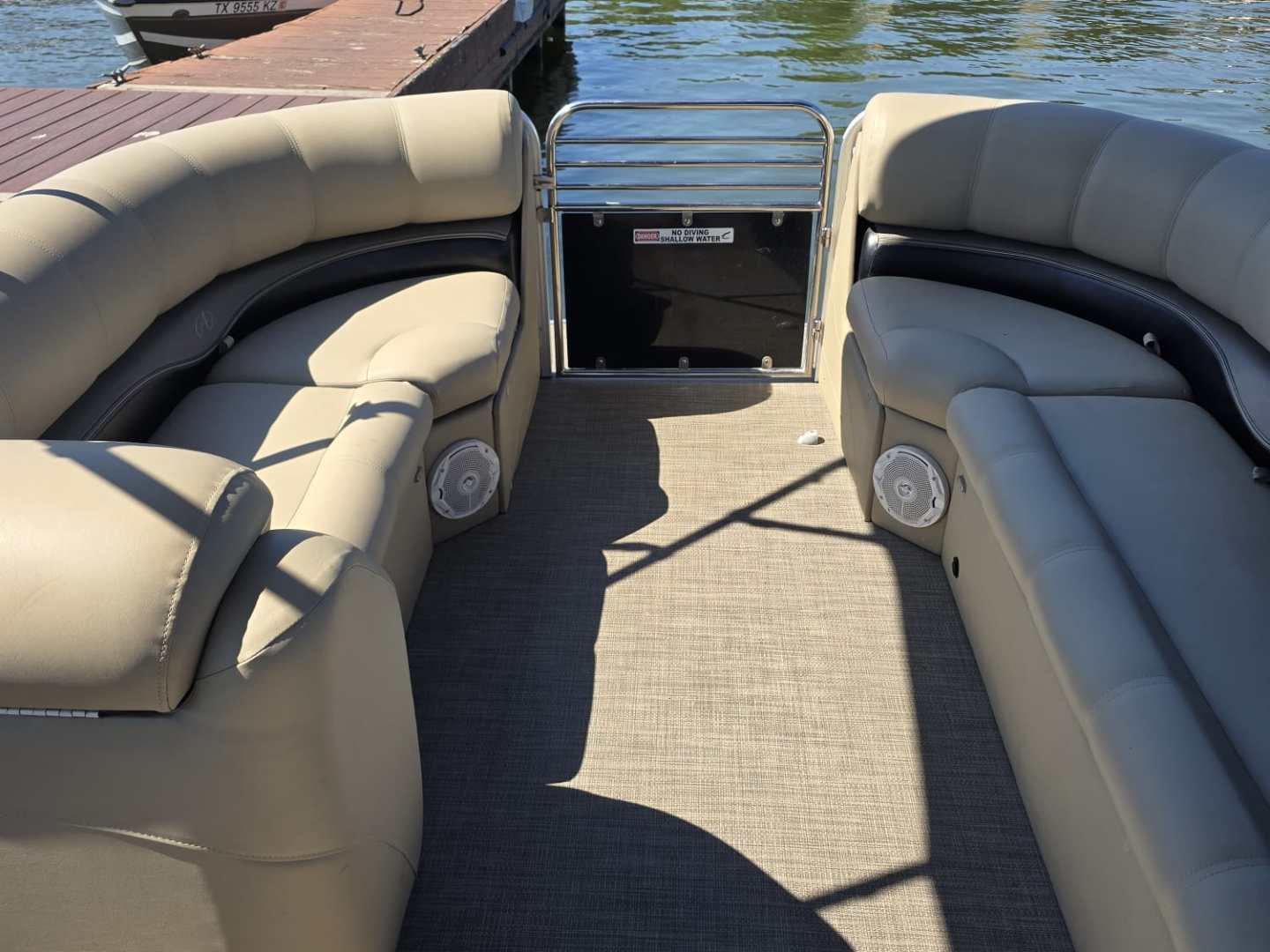 Pontoon boat interior with beige seats docked near a marina.