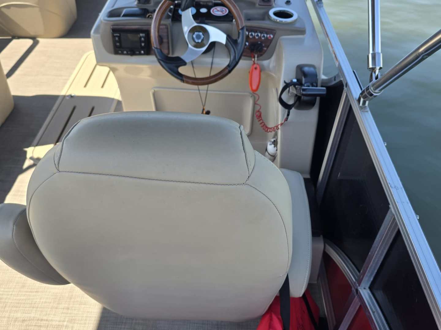 Boat cockpit with steering wheel, dashboard, and beige seats on a sunny day.