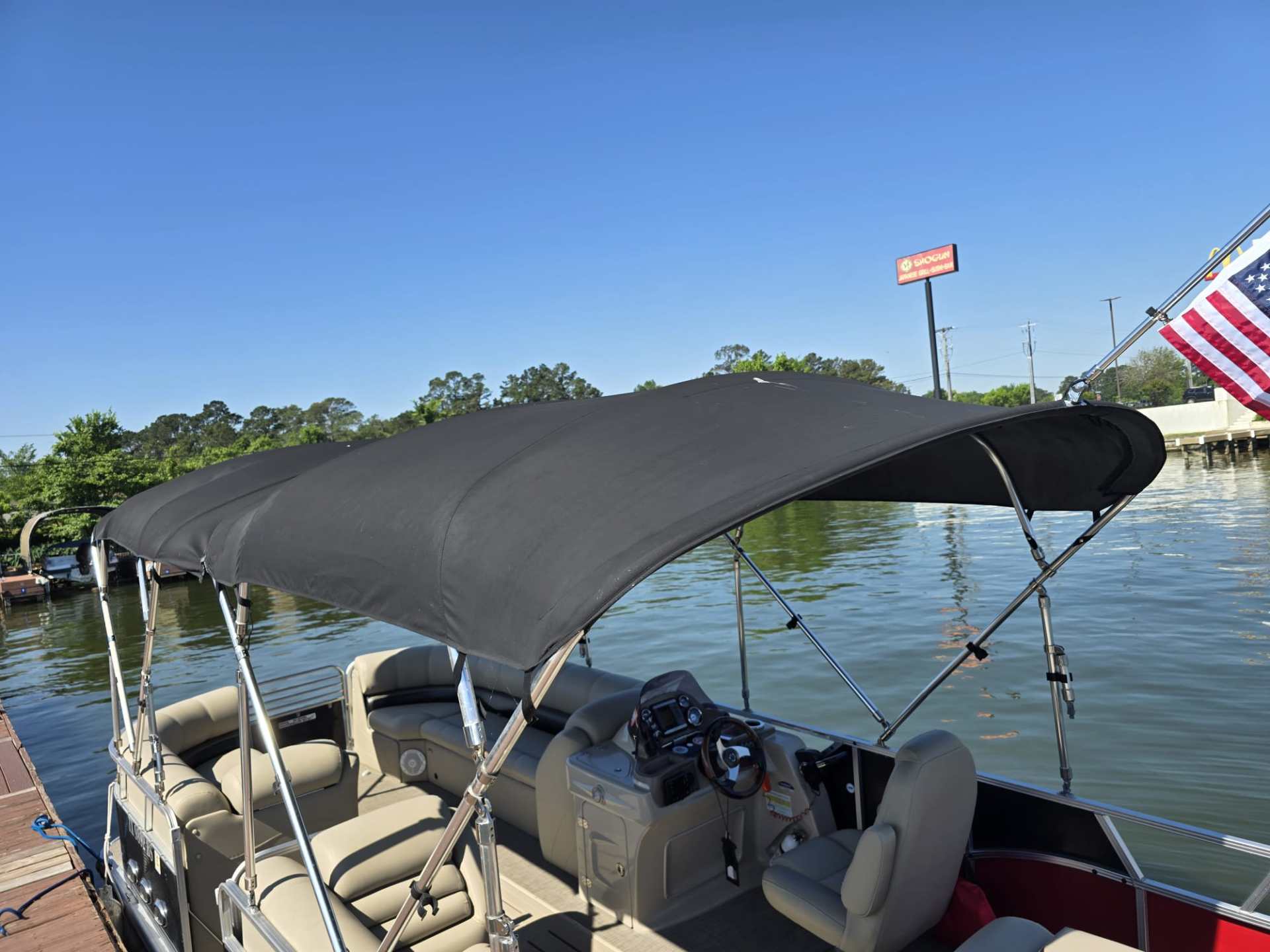 Pontoon boat with black canopy on a sunny day by a dock.