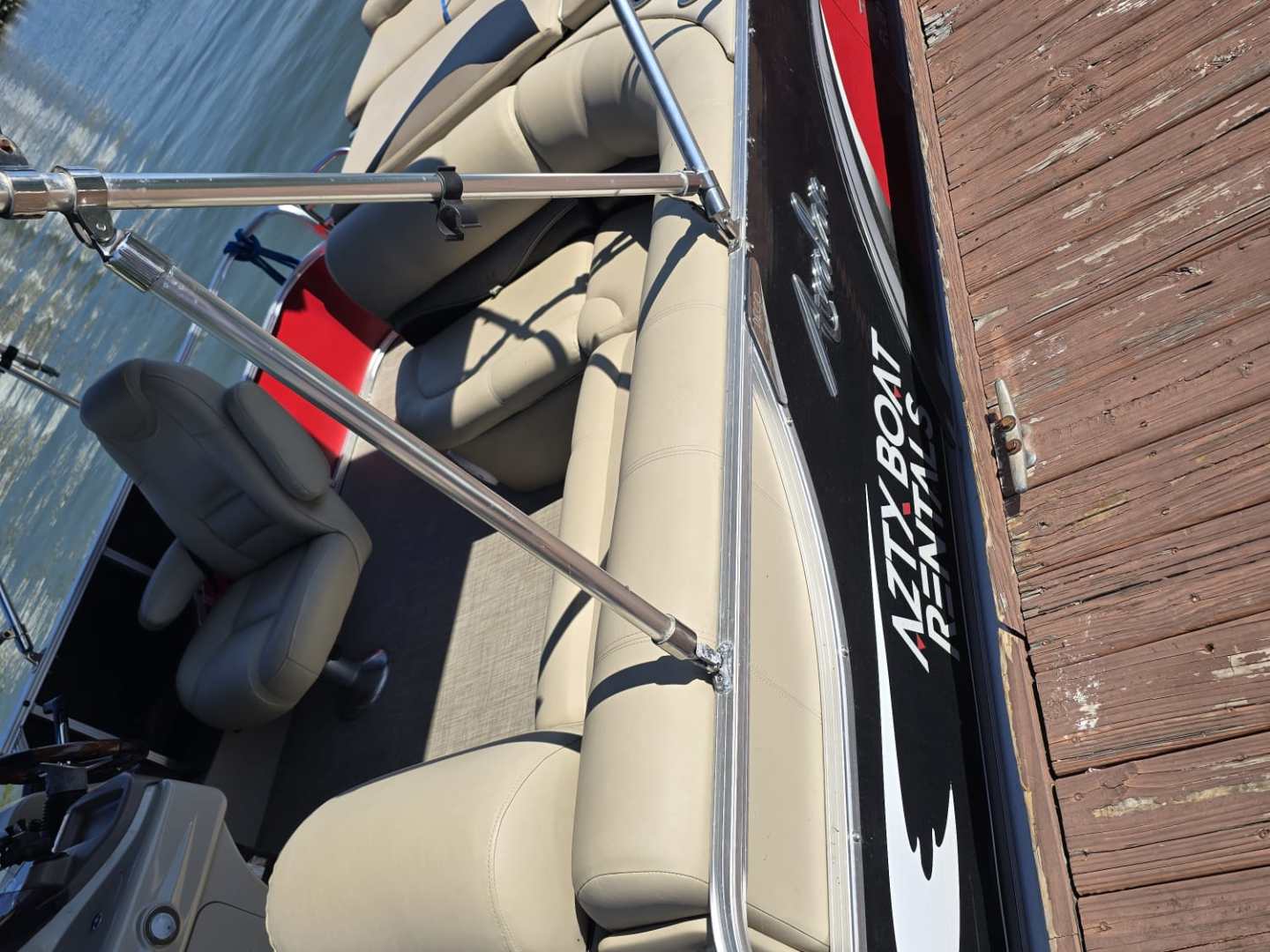 Pontoon boat moored to wooden dock on calm water.