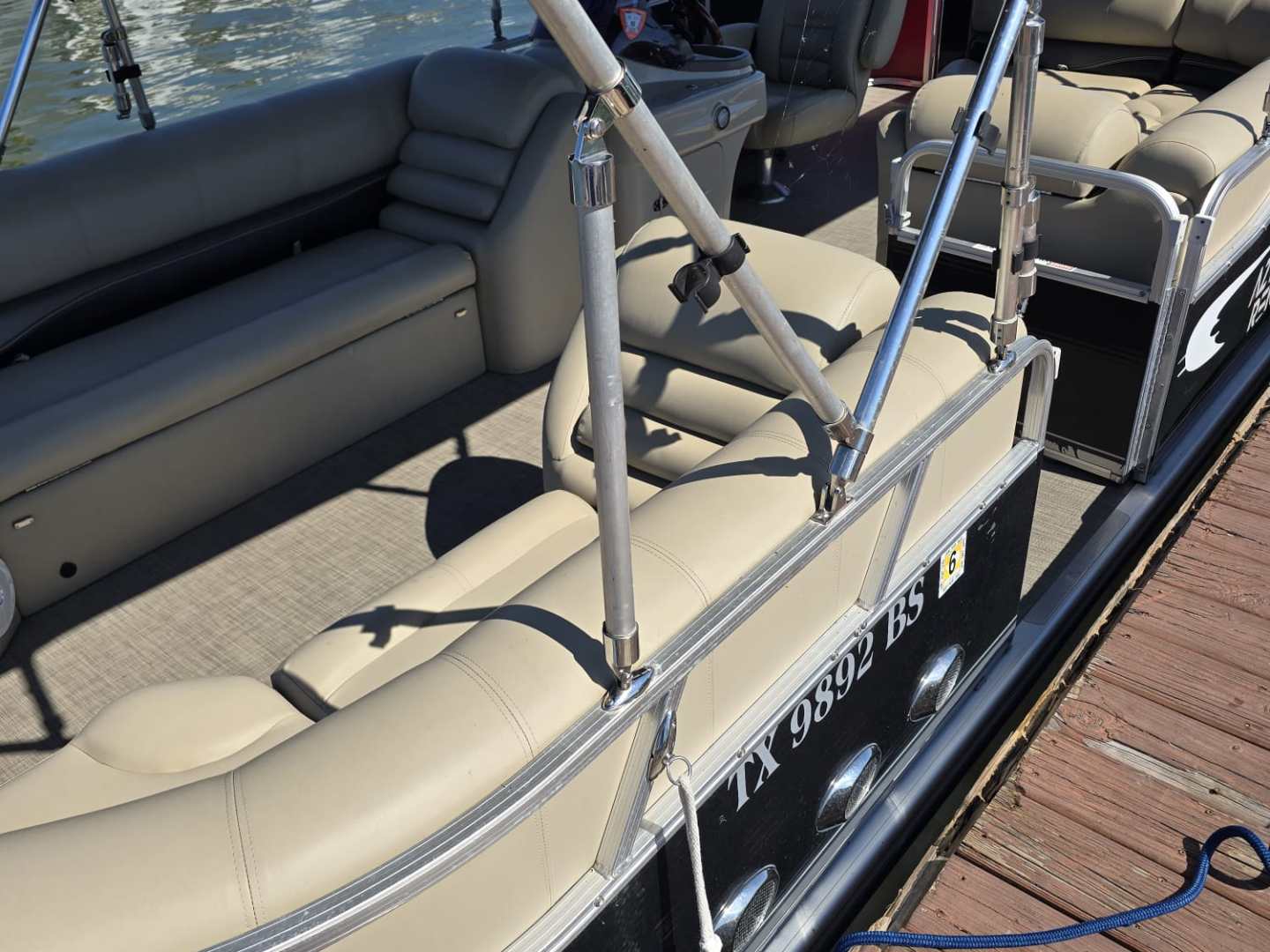 Pontoon boat docked on a sunny day, with beige seats and a canopy.