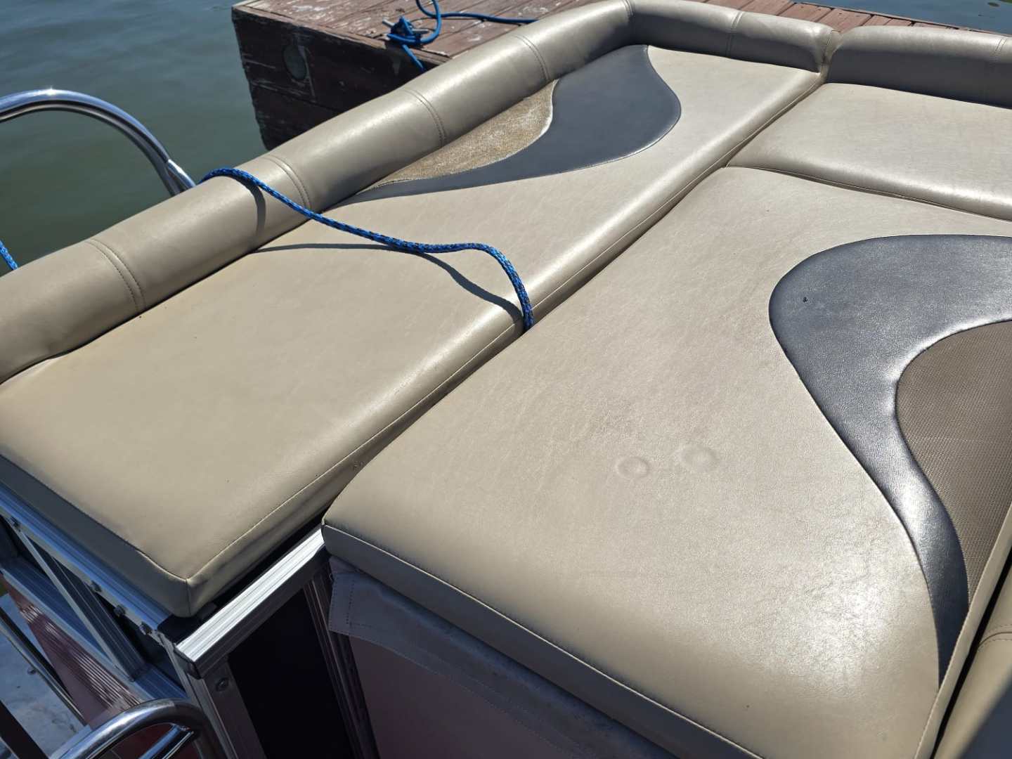 Boat seating area with tan cushions and blue rope by water and dock.