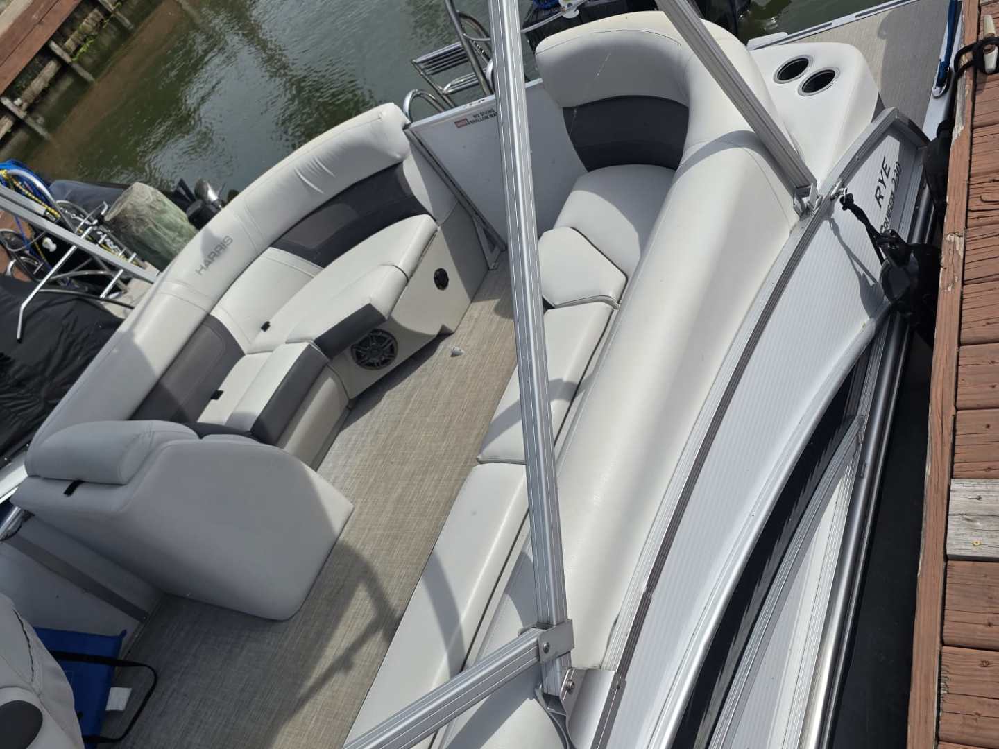 Pontoon boat docked by wooden pier with cushioned seating and canopy frame.