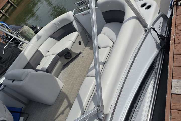 Pontoon boat docked by wooden pier with cushioned seating and canopy frame.