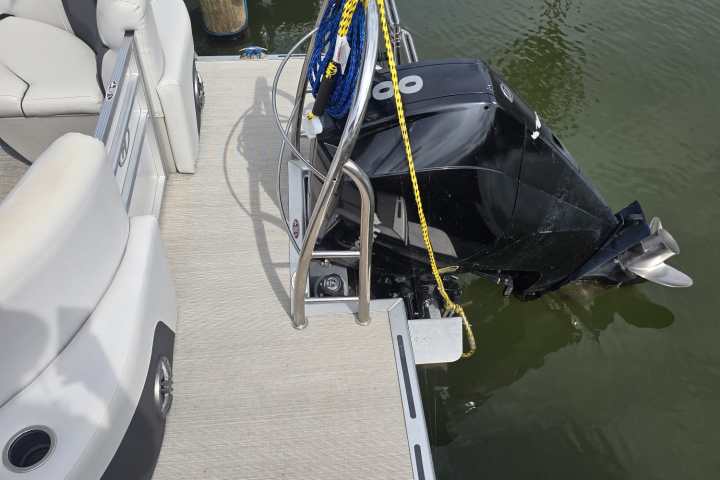 Pontoon boat with outboard motor docked on water.