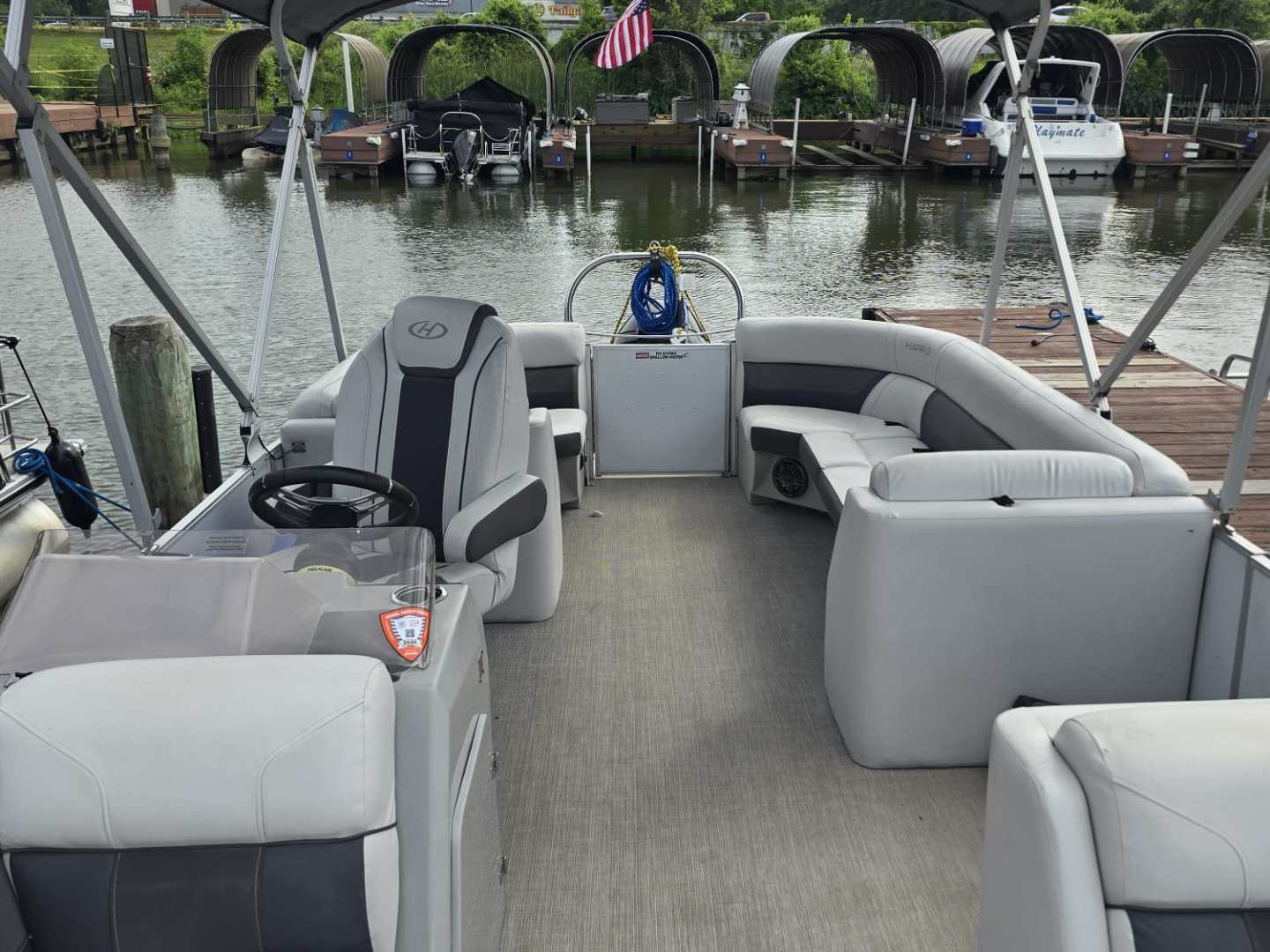 Empty pontoon boat docked, with canopy and seating, facing a harbor.