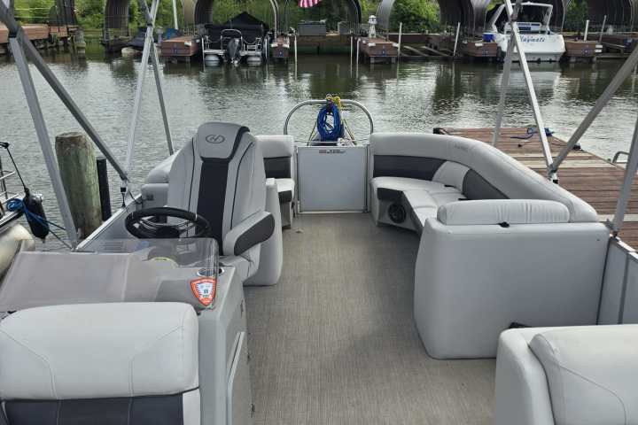Empty pontoon boat docked, with canopy and seating, facing a harbor.